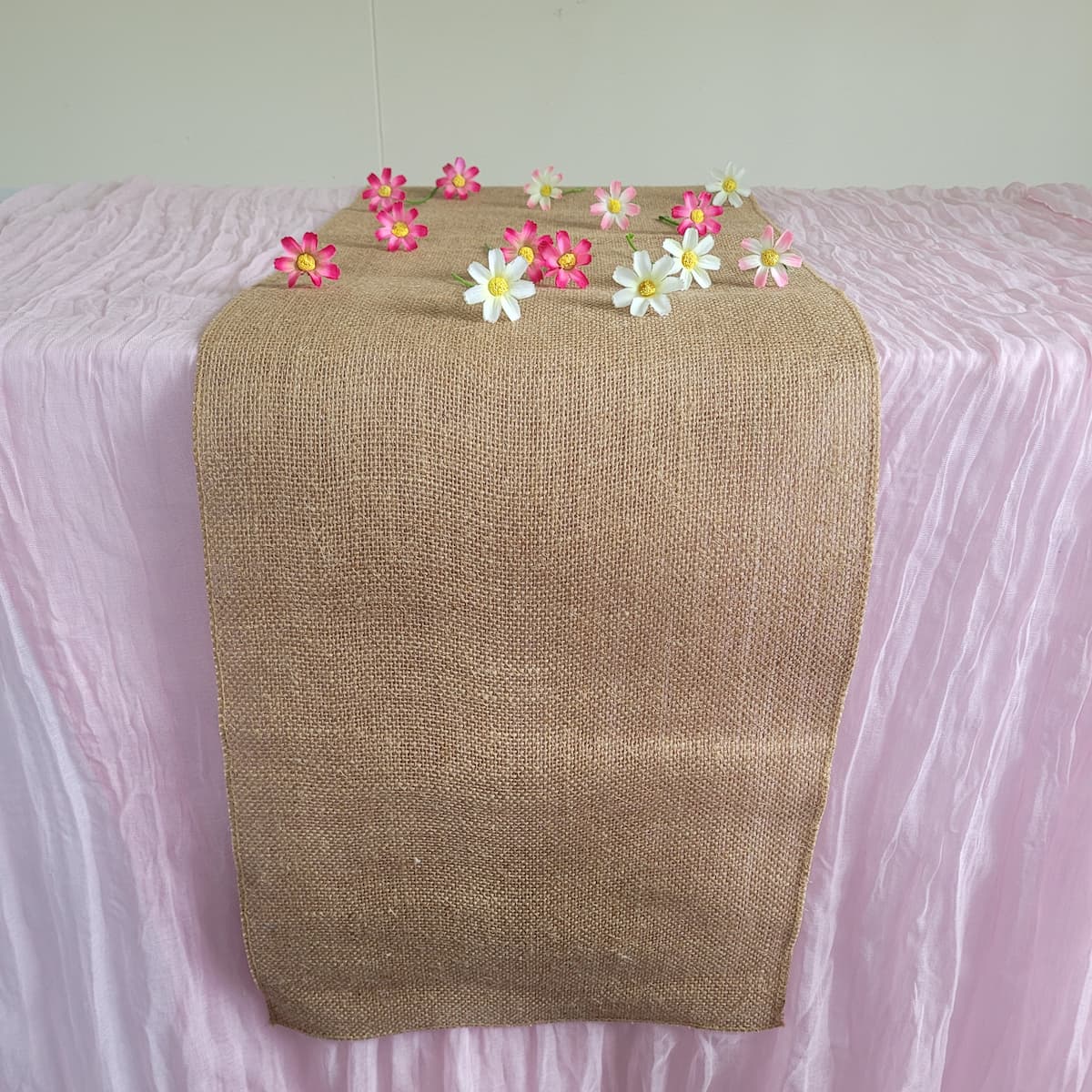 Hessian table runner on pink cheesecloth tablecloth with daisies